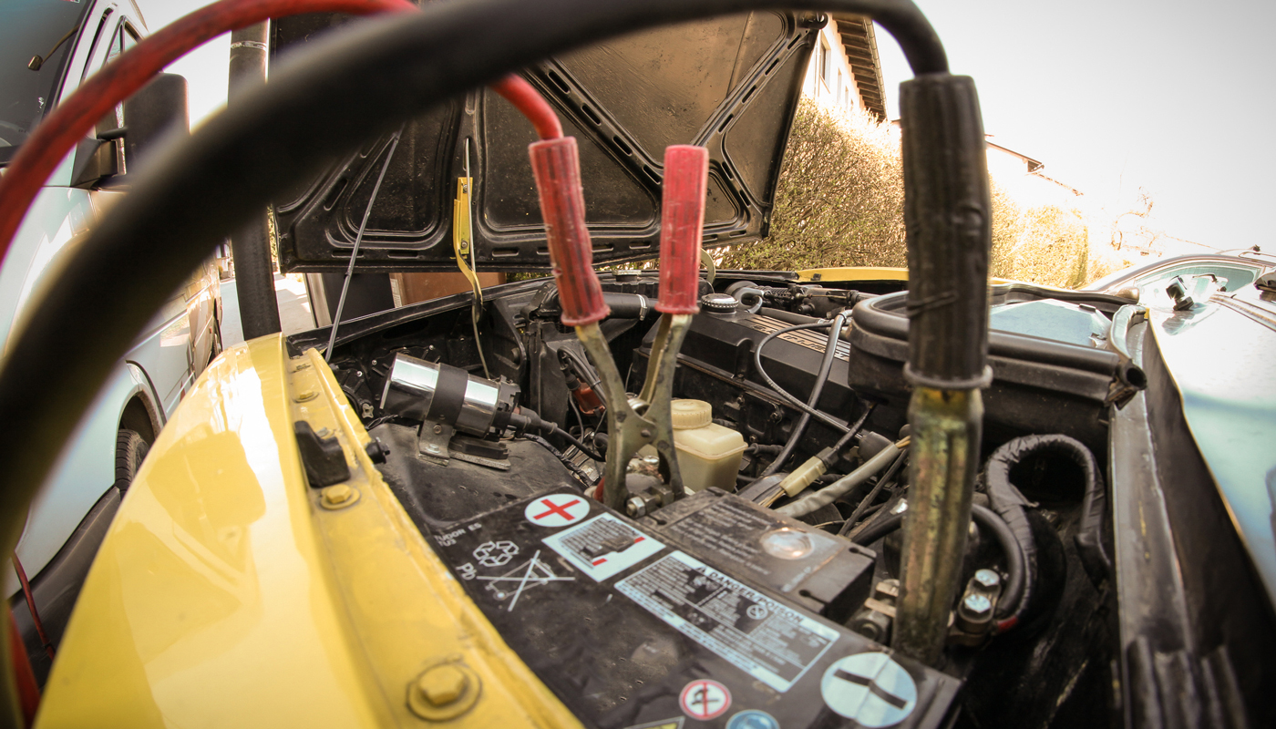 A pair of jumper or starter cables connected to a dead battery in a car.