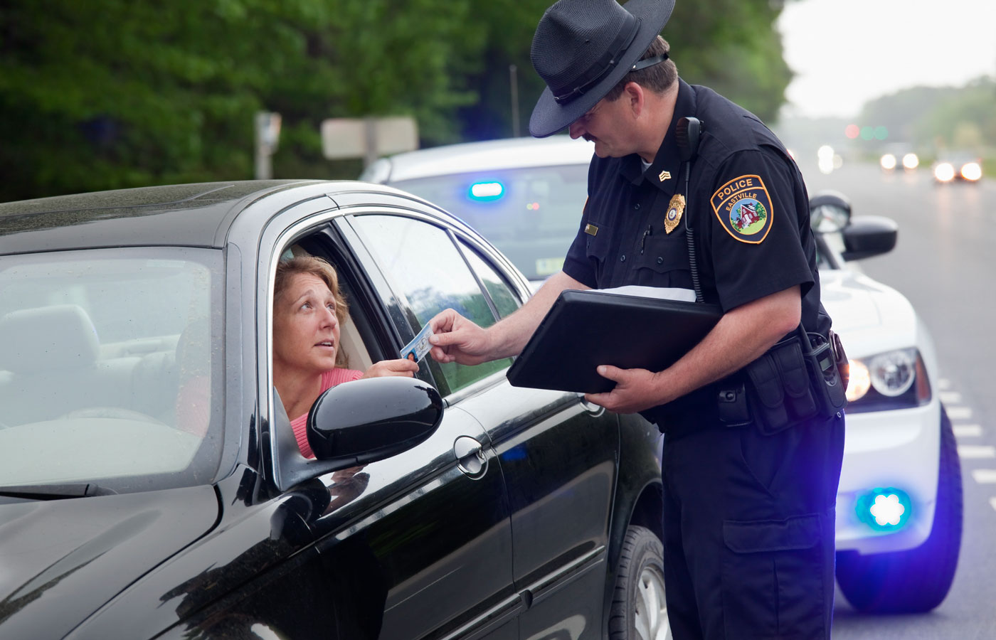 woman in her car with officer outside exchanging license.