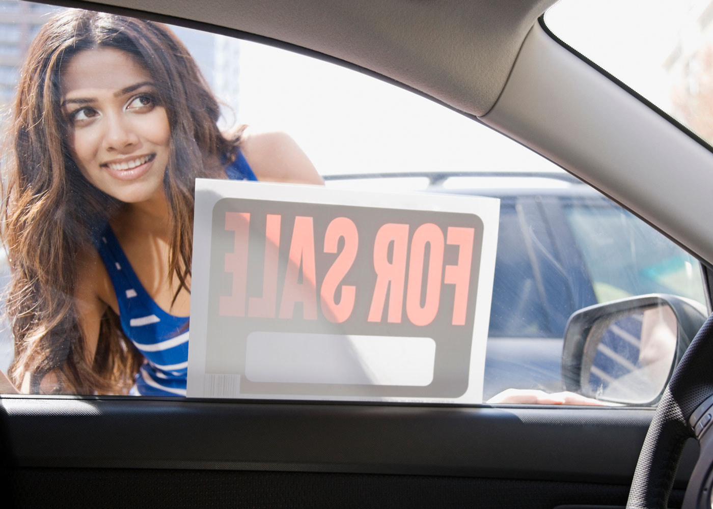 woman looking at FOR SALE sign on a car