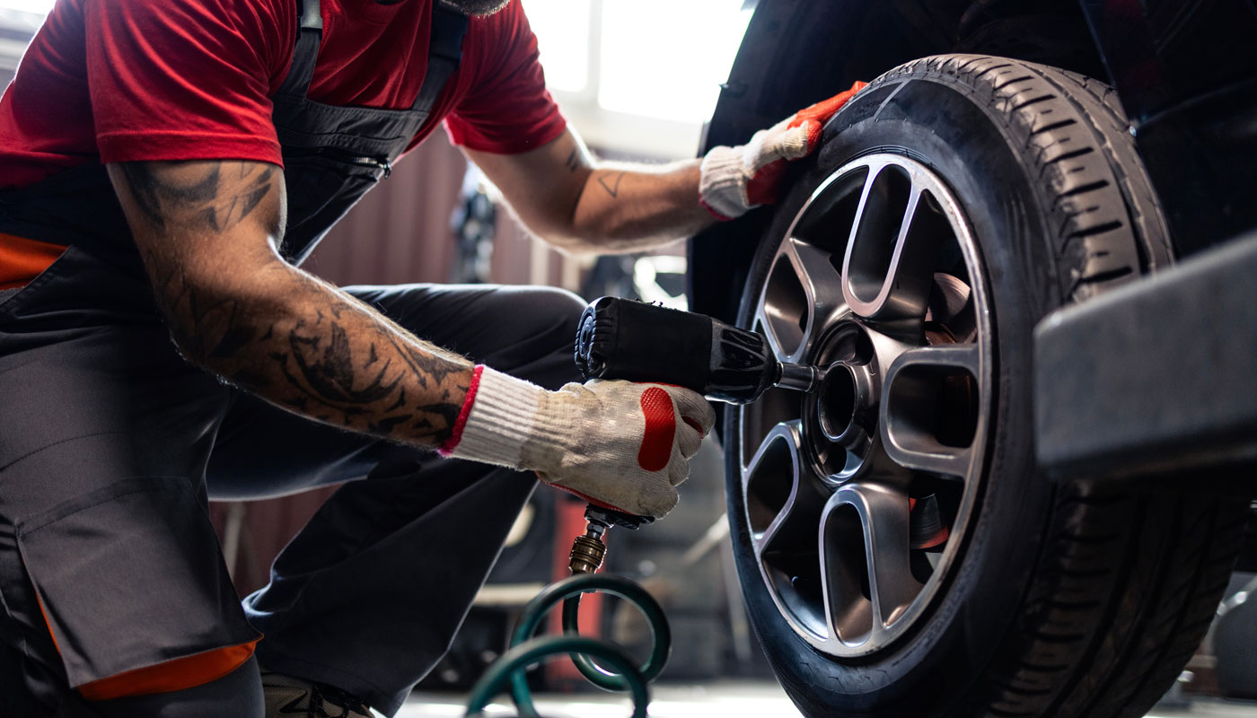 Tire shop mechanic using pneumatic screw gun to remove the wheel. Replacing tires on the car.