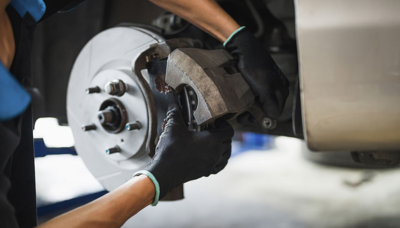 Auto mechanic installing car front brake caliper and brake pads.