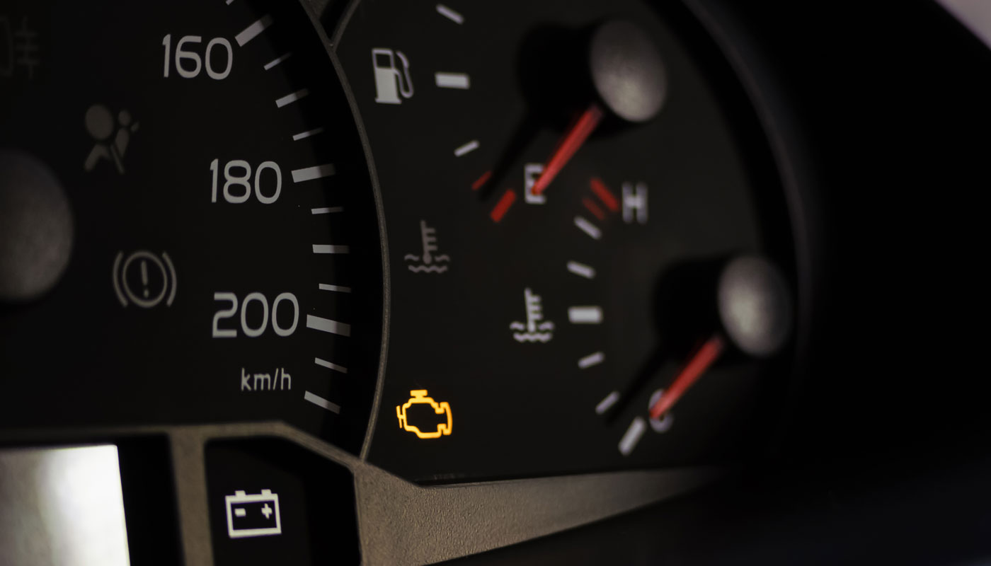 Yellow lit engine error sign on car dashboard close up