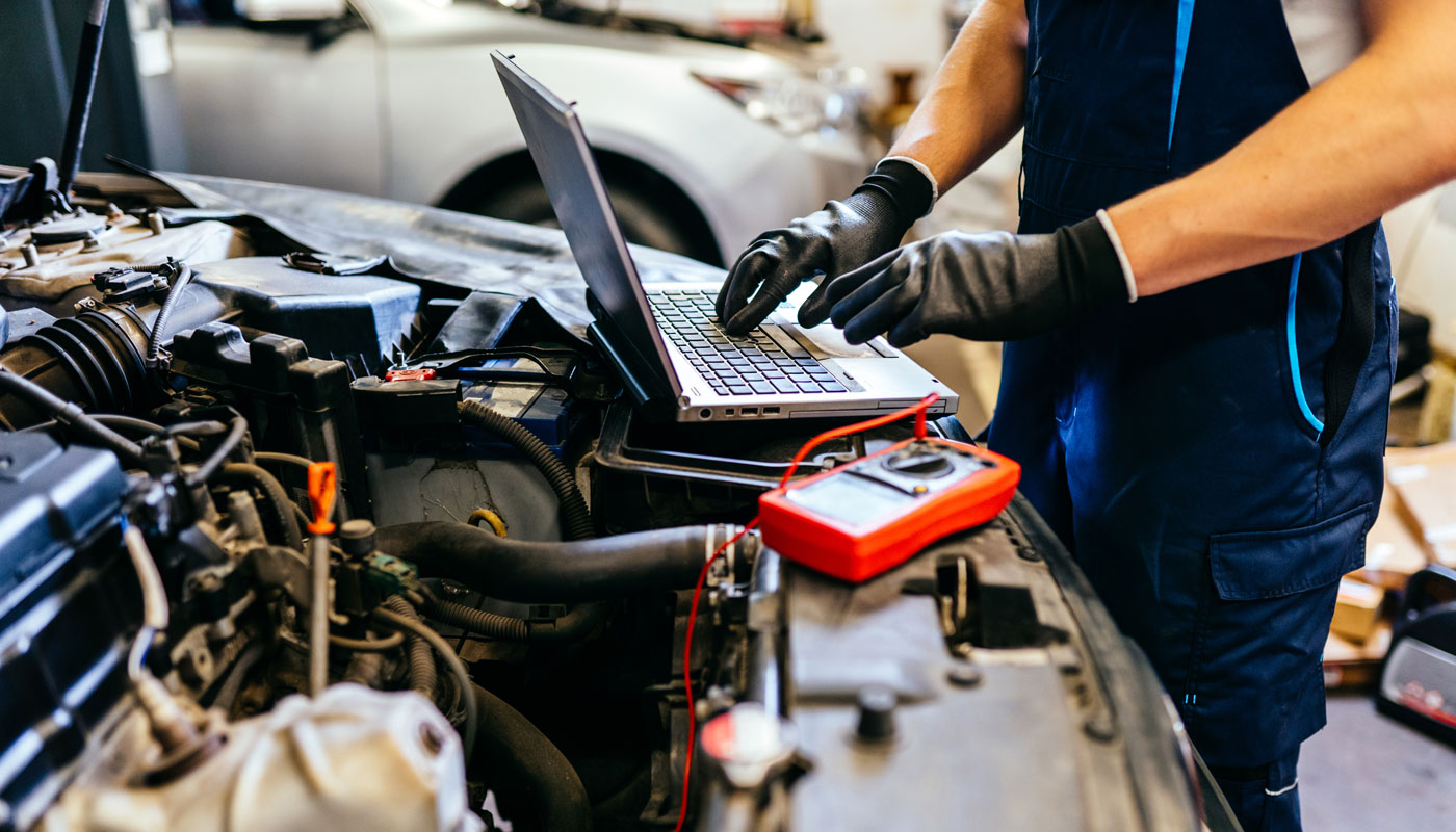 Car technician using computer in auto repair shop.