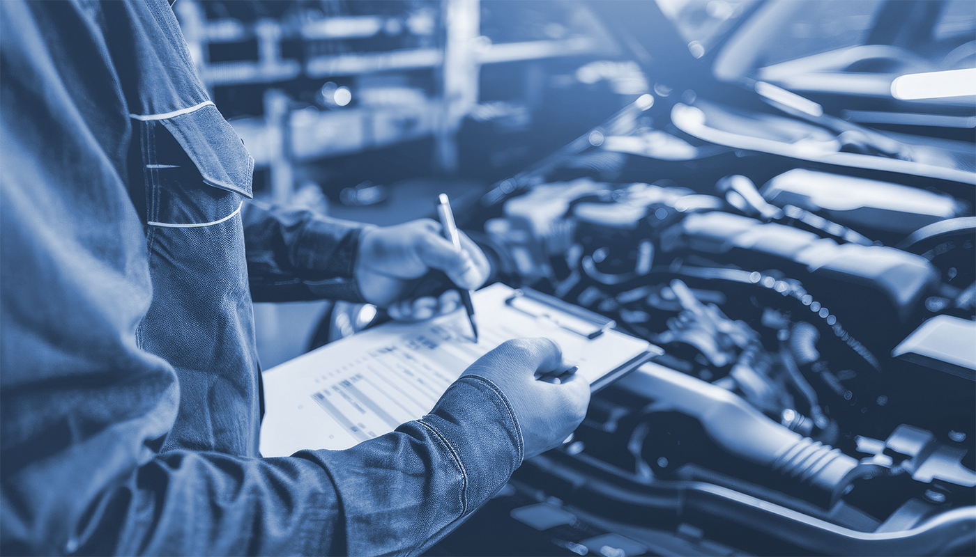 An auto repairman writes a job checklist on a clipboard while inspecting an engine to estimate repairs and maintenance at a vehicle garage.