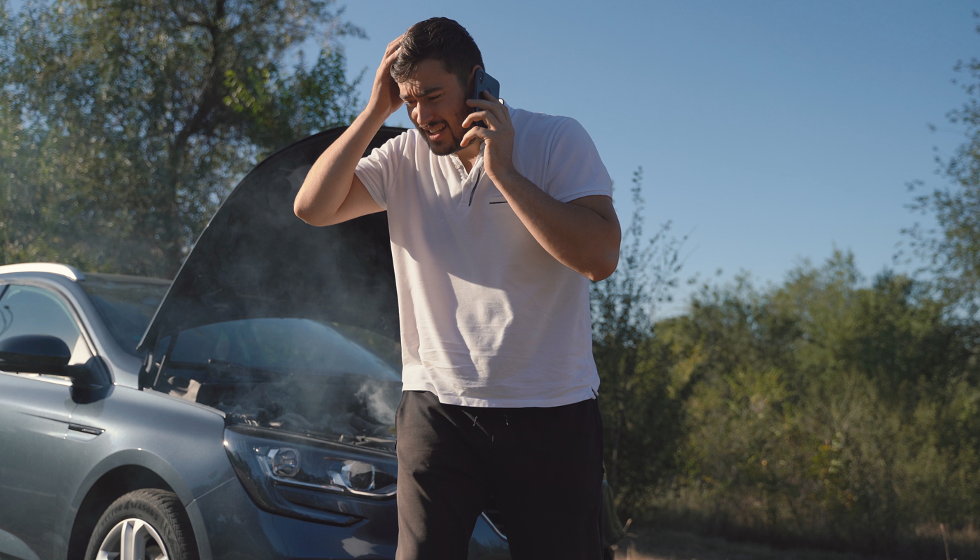 Man on his mobile phone with his car on side of road and hood up in the background 