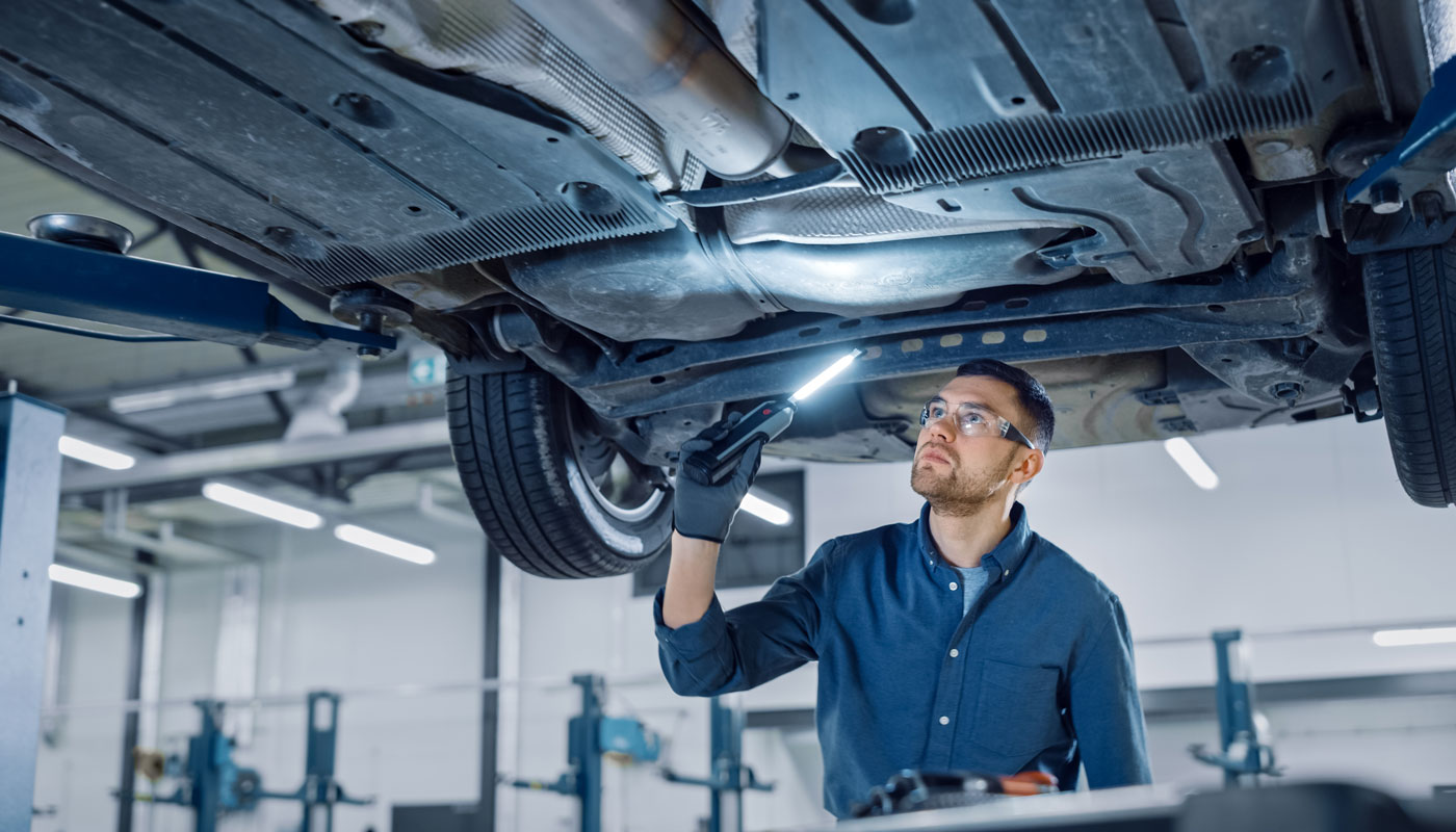 Car Mechanic is Investigating Under a Vehicle on a Lift in Service