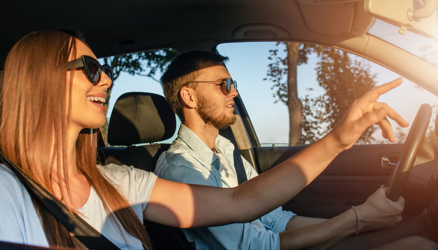 Young Woman in Car is Pointing at Something Interesting; both male and female wearing sunglasses