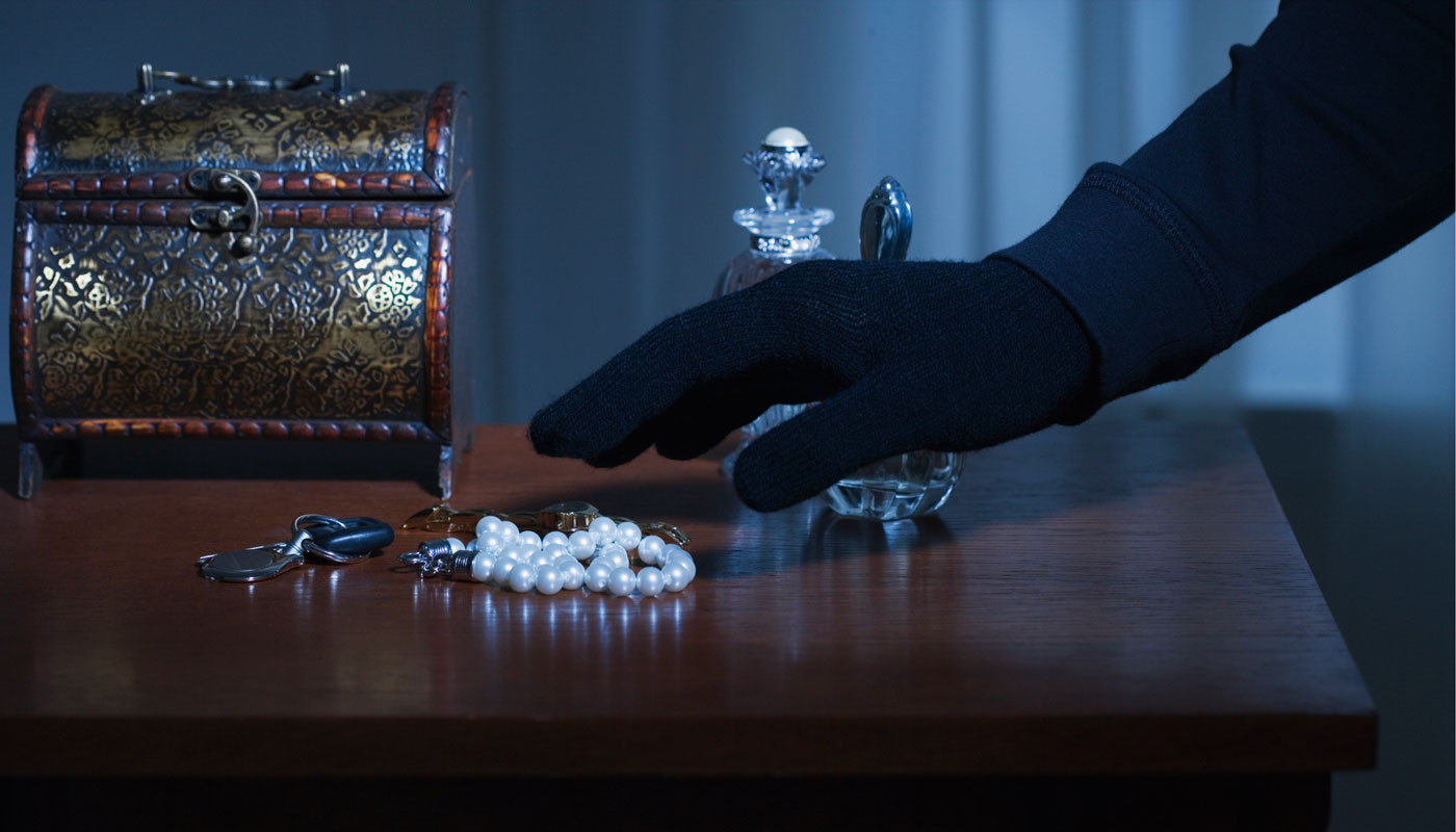 hand with black glove shown stealing jewelry from a dresser