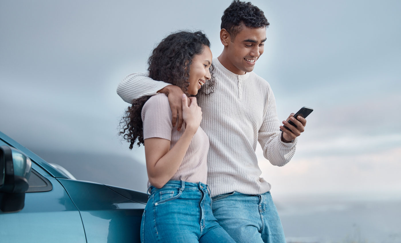 Couple looking at cell phone next to their car.