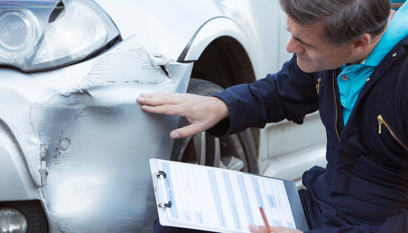 Auto Workshop Mechanic Inspecting Damage To Car And Filling In Repair Estimate