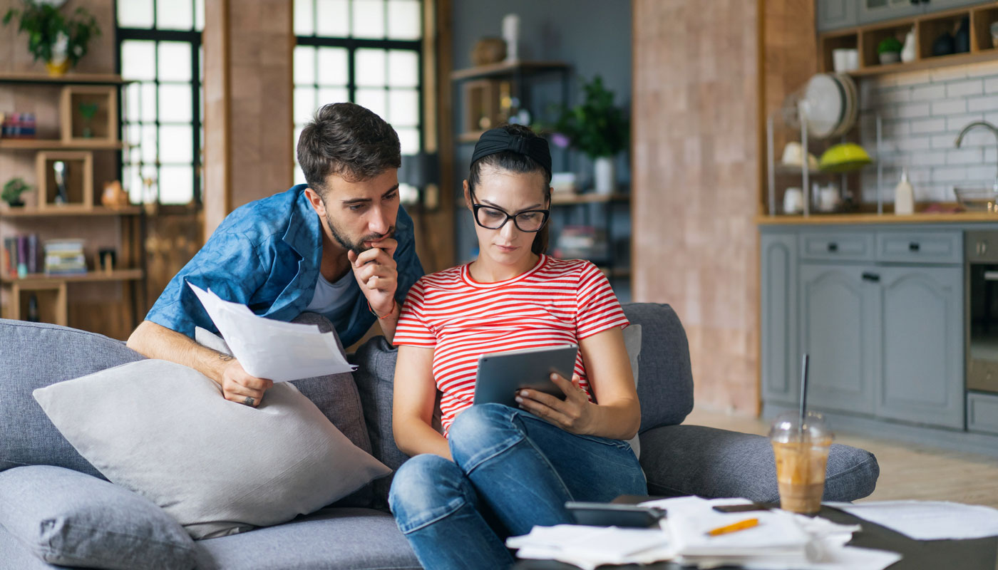 Couple on couch reviewing paperwork and tablet.