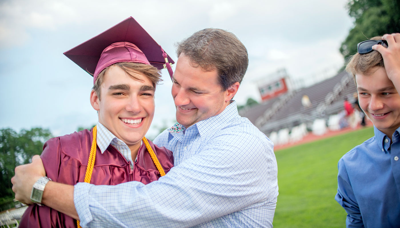 Graduate being hugged by his dad with brother standing nearby