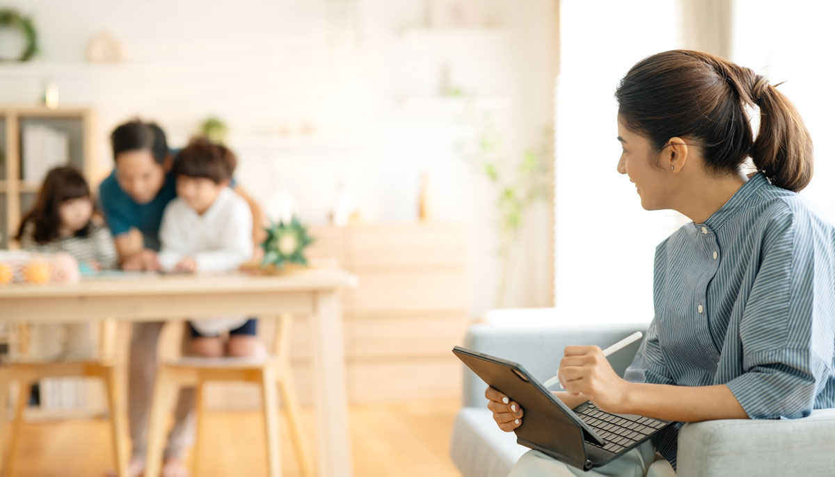 Mother on her laptop with husband and kids in background