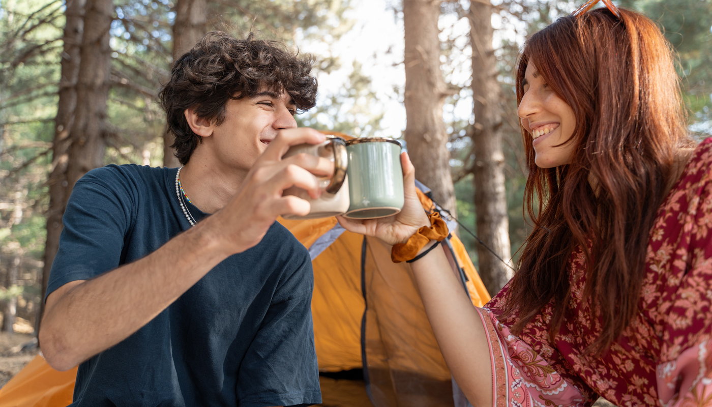 Young couple enjoying coffee while camping in forest, outdoor lifestyle concept