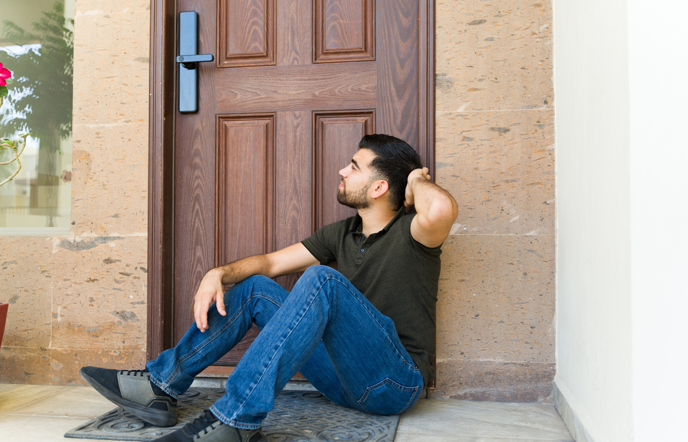 Young man locked out of his house and sitting and waiting next to his door 