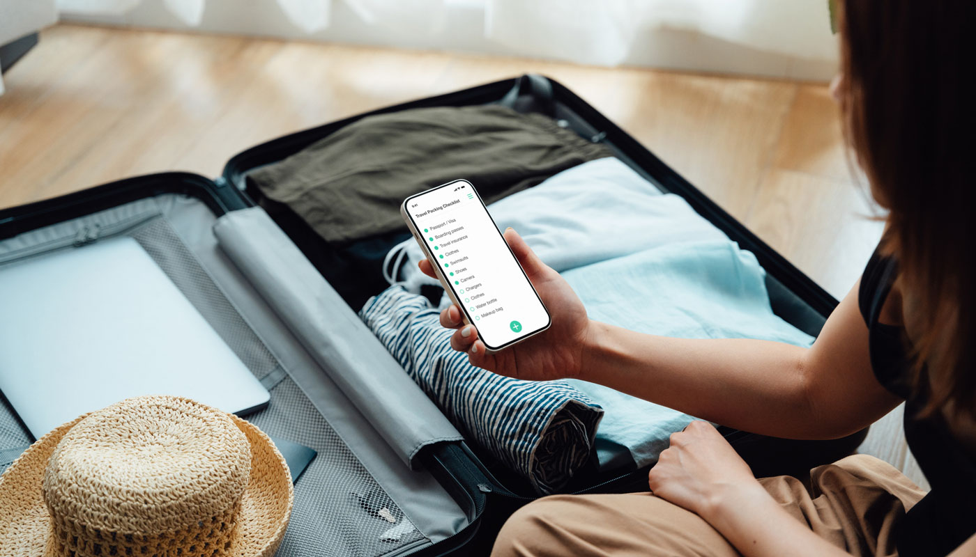 A woman looking at a smartphone while packing a suitcase.