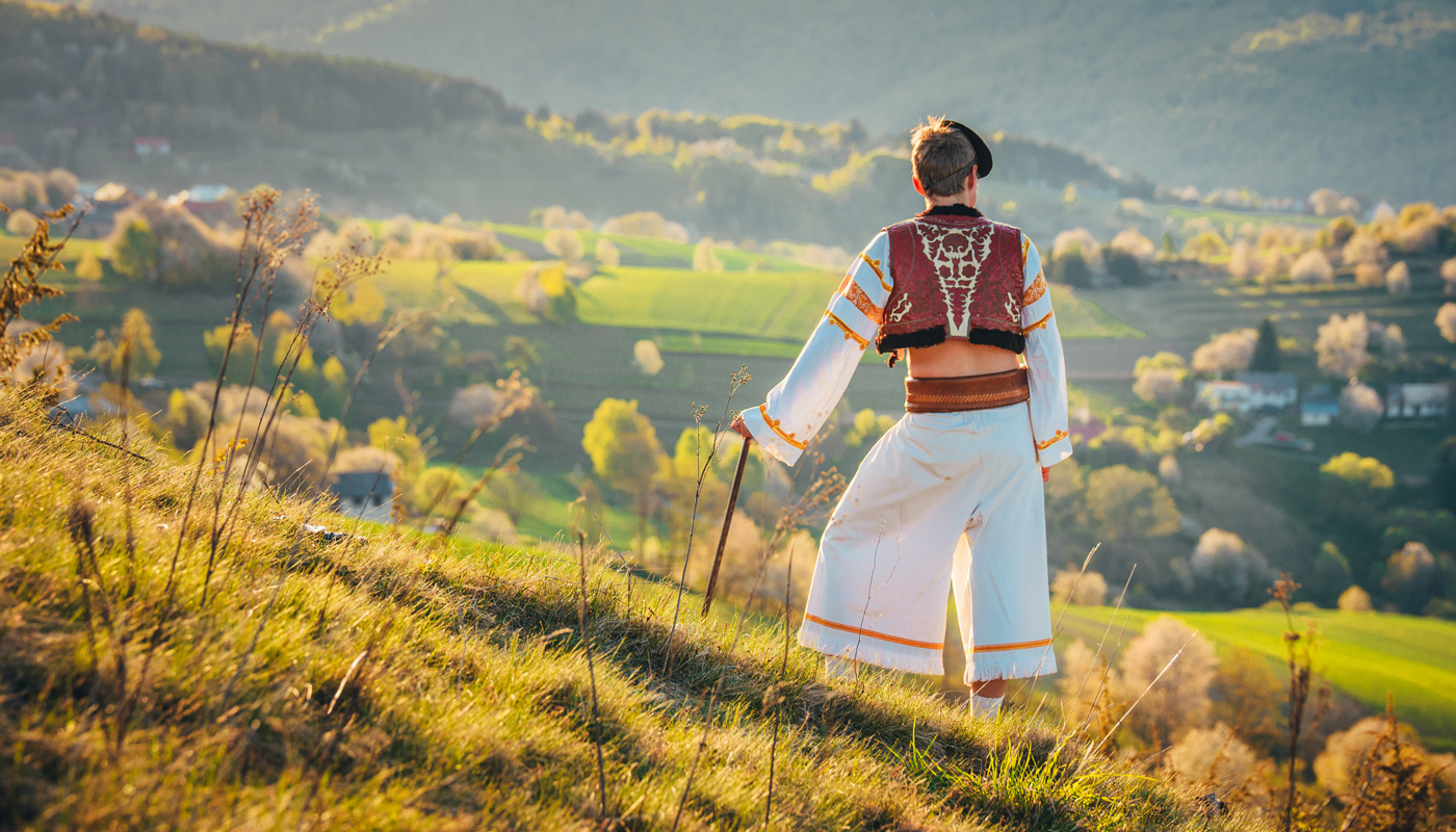 A young man in a Slovak folk costume looks at the spring landscape in the village of Hrinova in Slovakia