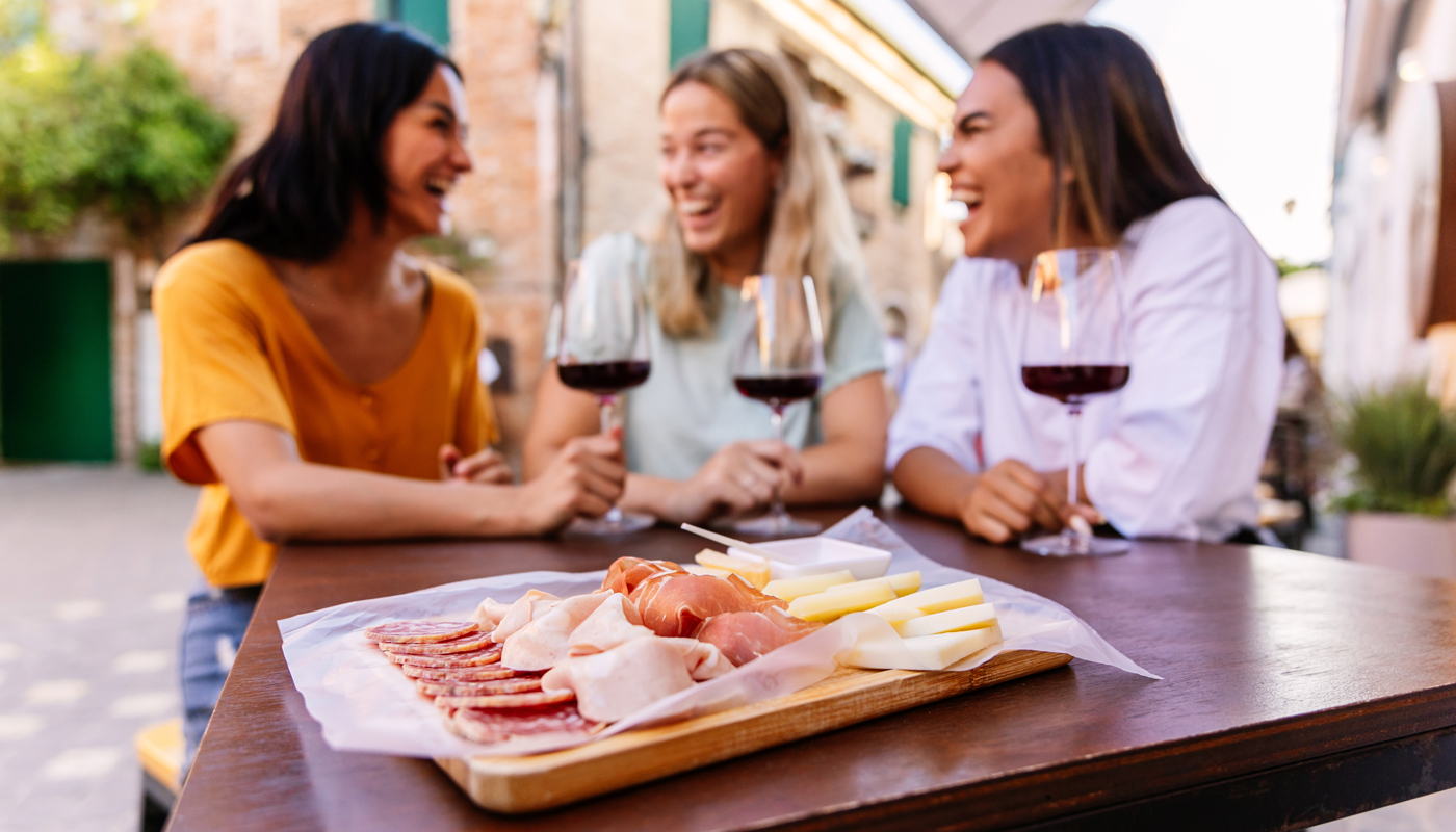 Three happy diverse women having fun together enjoying red wine at restaurant