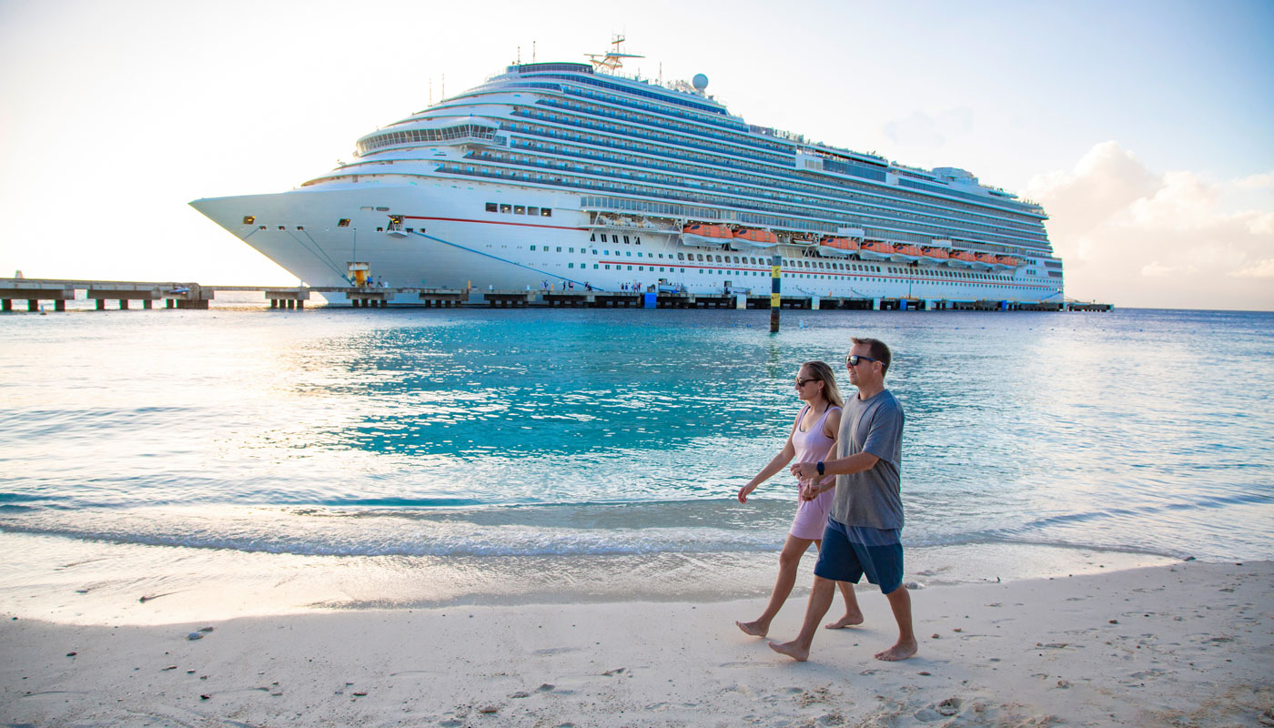 couple holding hands and walking together on a beach with a Cruise ship in the background