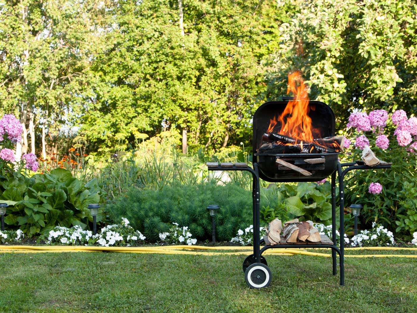 A backyard BBQ grill that is on fire with flames shooting out of the lid.