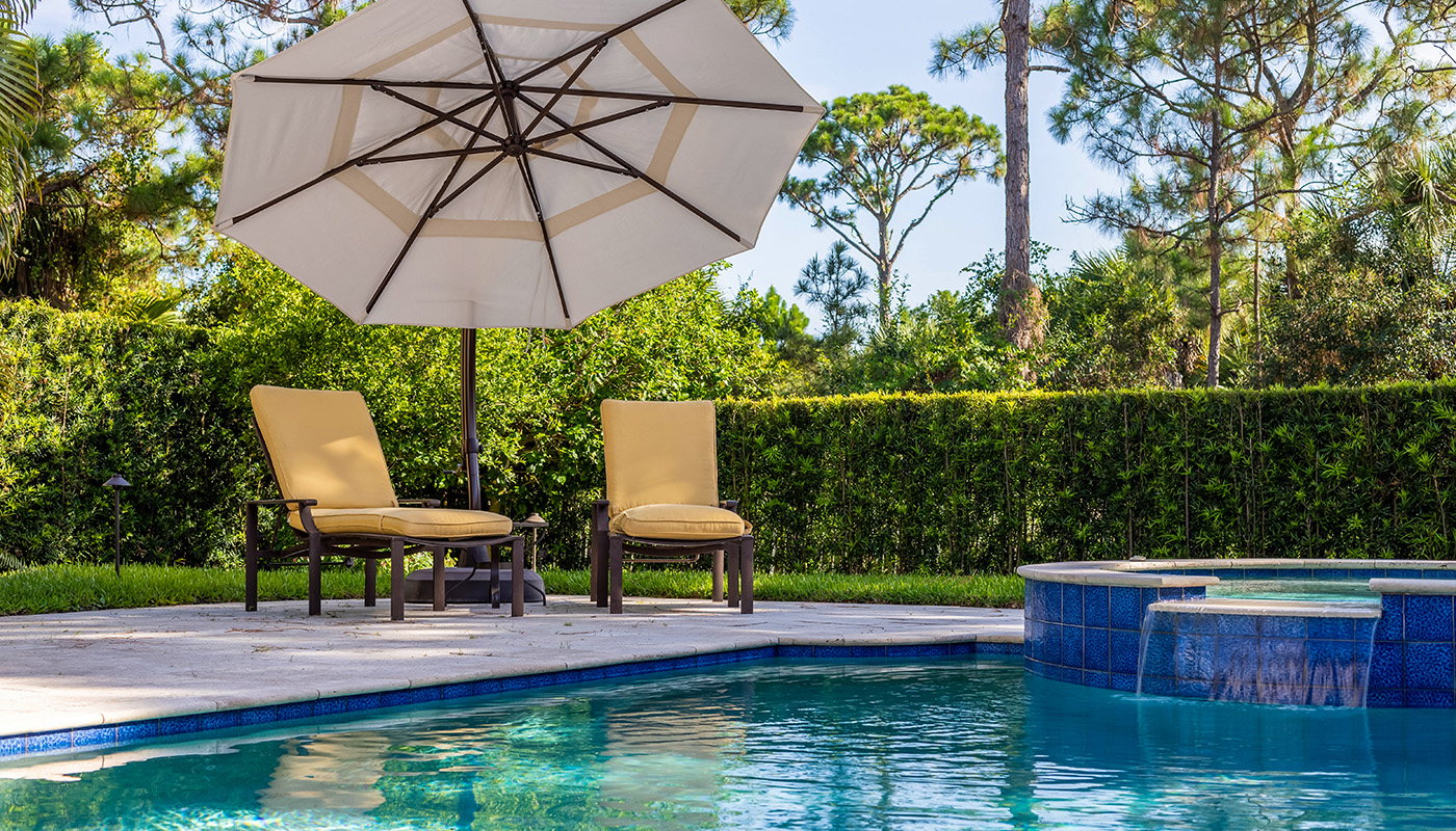 Two lounge chairs under an umbrella beside a backyard pool.