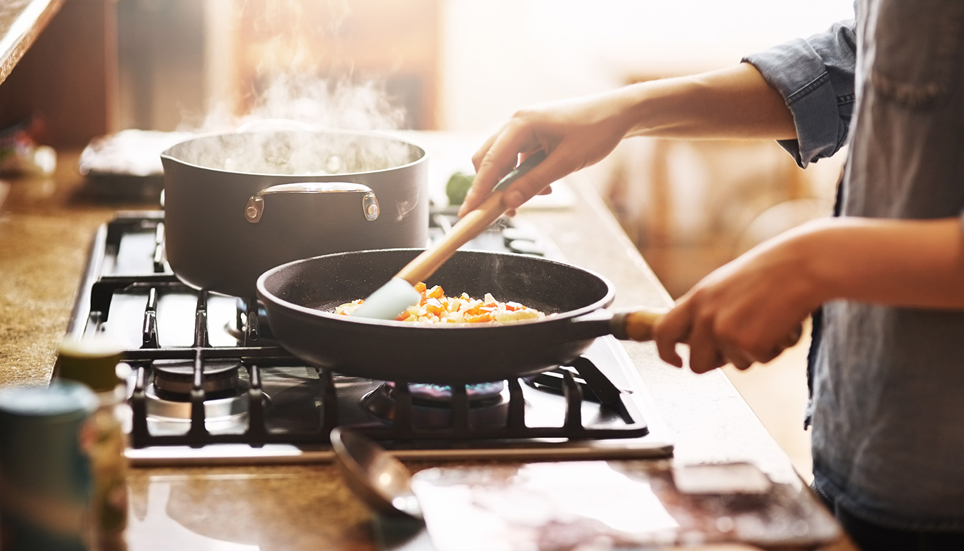 A close up view of someone preparing a meal in a skillet on a gas range.