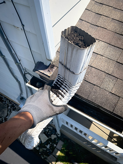 Gloved hand holding clogged gutter downspout