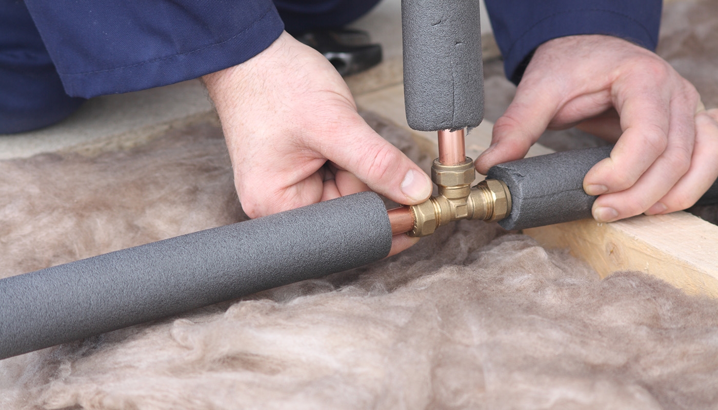 Closeup photo of Caucasian hands adding insulation to copper pipes