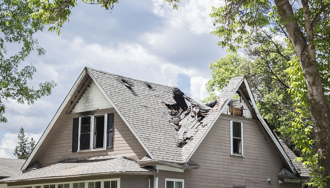 Photo of a roof of a house that has burned and collapsed under blue sky with clouds