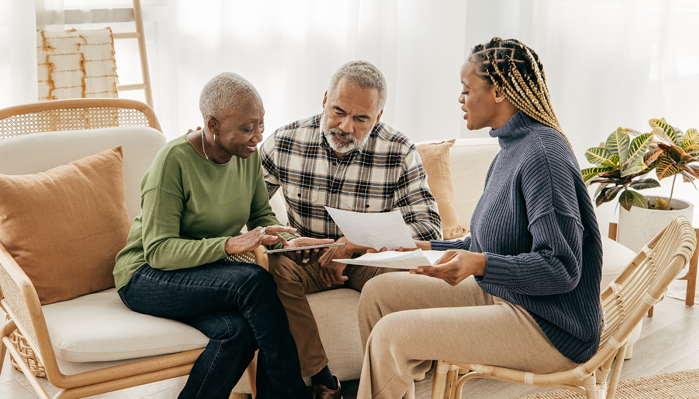 Older African American couple discussing paperwork with younger African American woman in bright sunny room