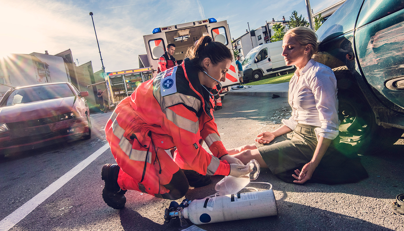 A paramedic tends to a woman sitting beside a vehicle on the side of the road.