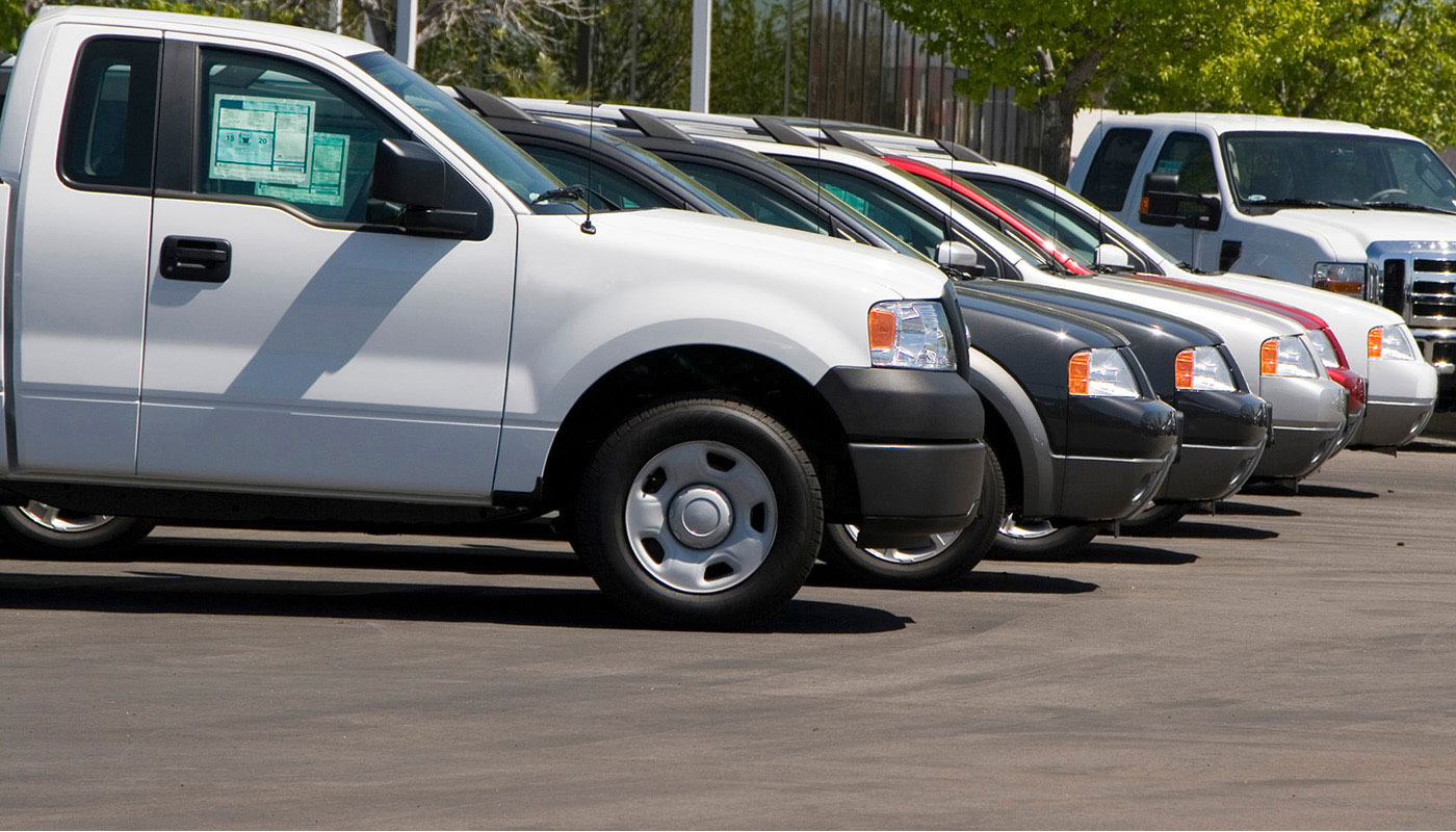 Seven vehicles sit in a row in a car dealership lot.