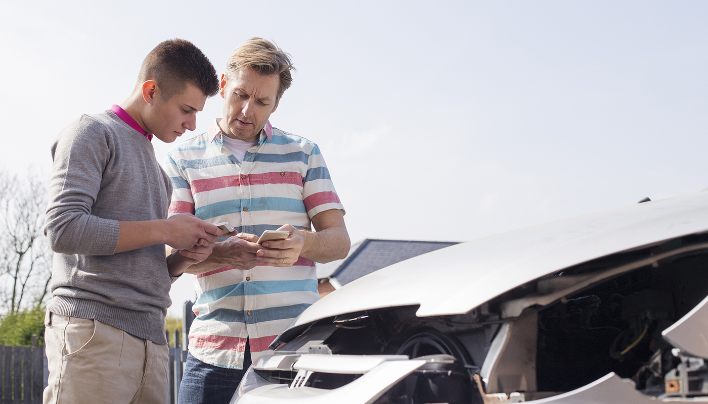 Two men standing in front of a car are discussing auto insurance. 