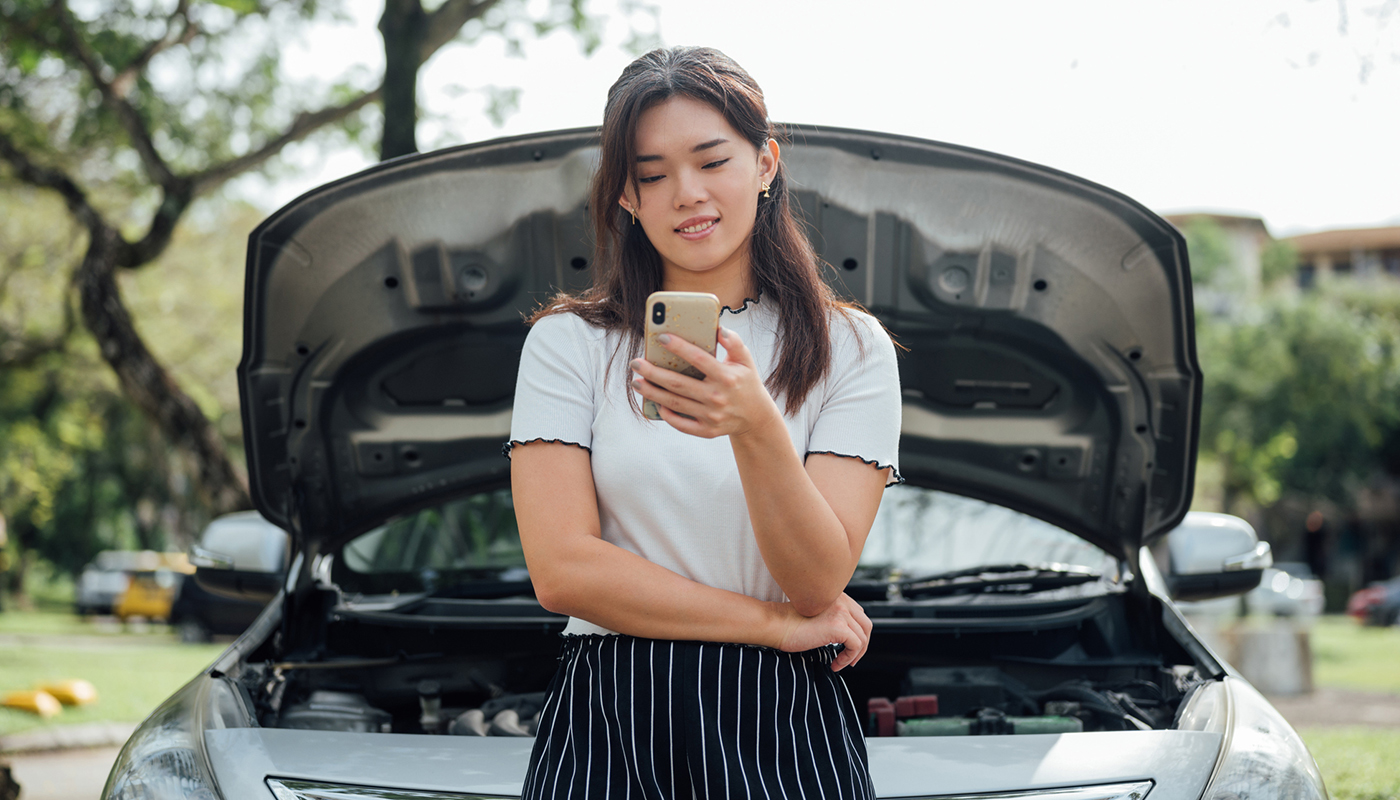 A young woman looking at her mobile phone stand on front of her parked car.