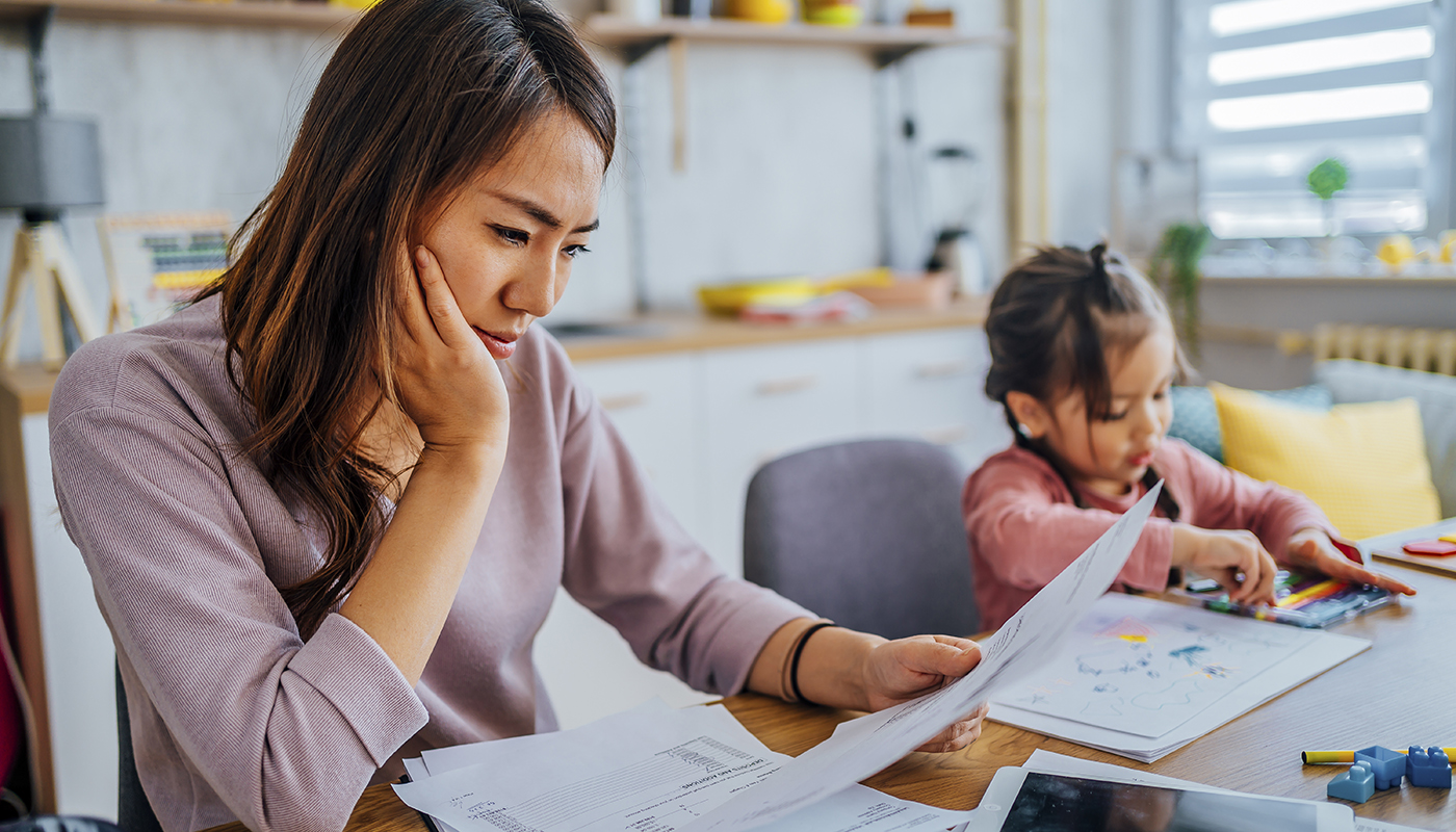 Young mother looking over bills with her child at the kitchen table.