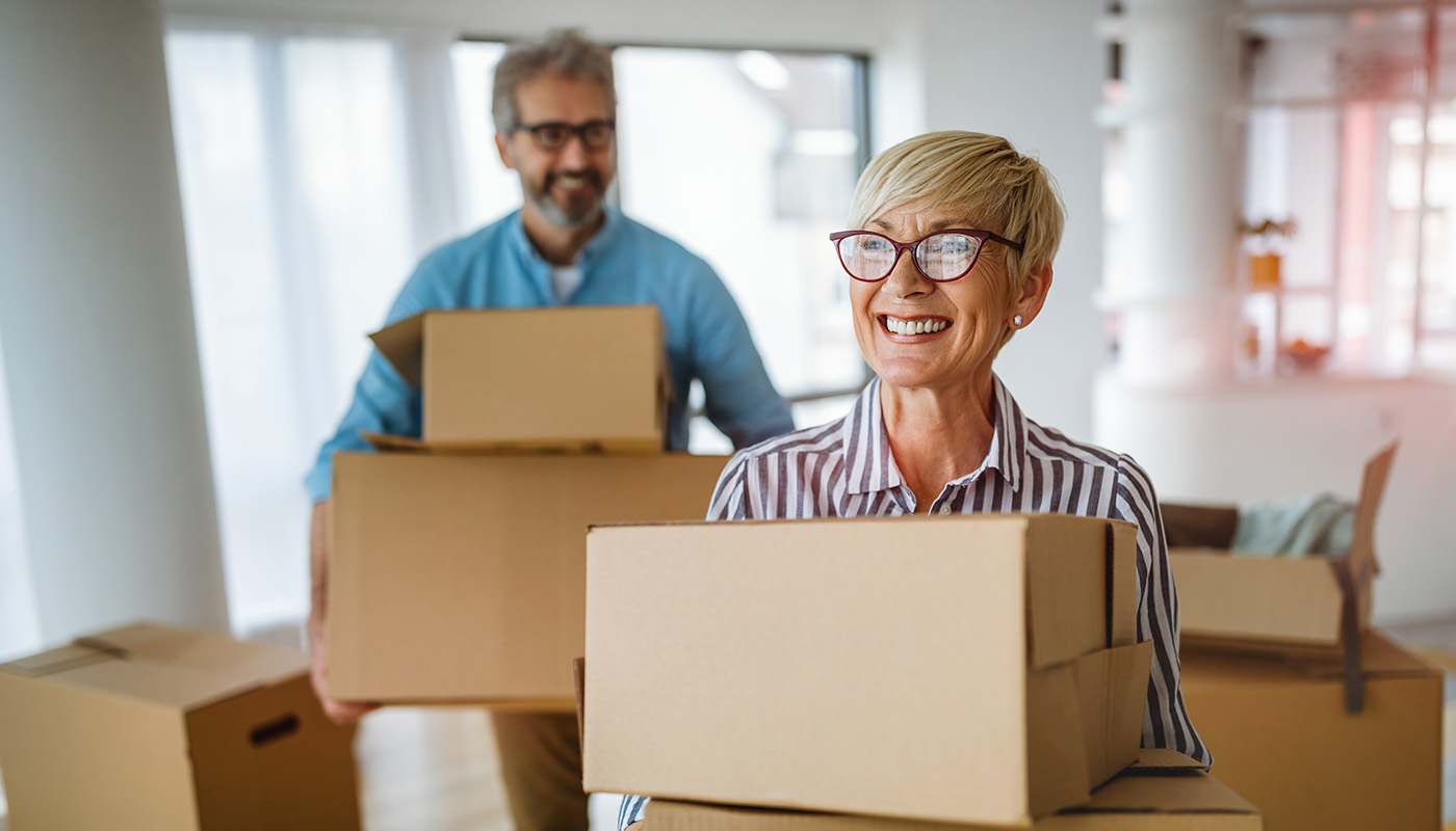 Couple smiling and carrying moving boxes inside home