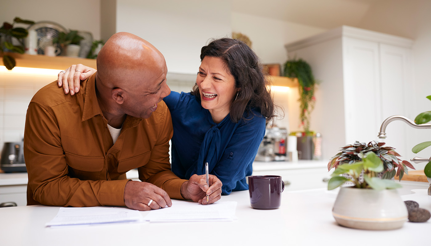 Couple standing at kitchen counter smiling and writing down notes
