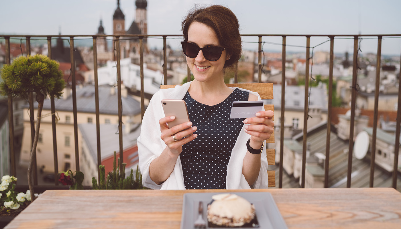 Woman dining outside at rooftop restaurant looking at smartphone and holding credit card