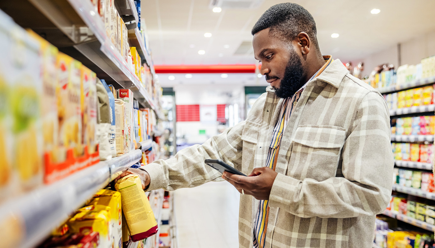 A man reaches for an item in a grocery aisle while looking at his cellphone