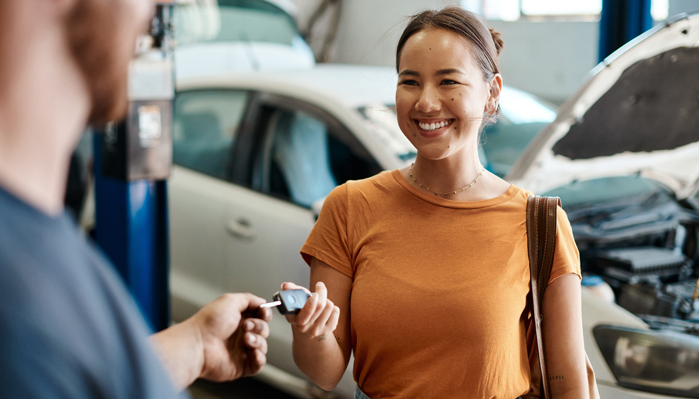 A smiling woman hands a man a key to a vehicle