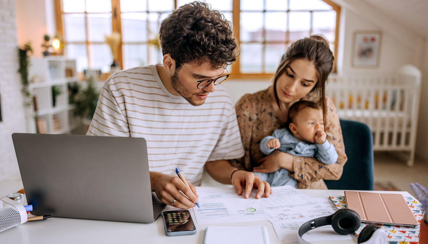 A man and a woman with baby sit in front of a laptop with paperwork