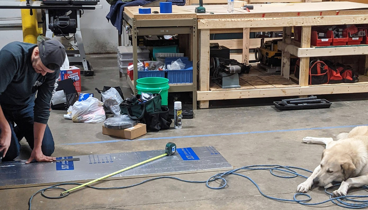 Jon cut pieces of Polyiso board, which he installed inside the van's subfloor frame. This insulation layer would live beneath the plywood and vinyl plank flooring. A dog, meanwhile, steadies the wires.