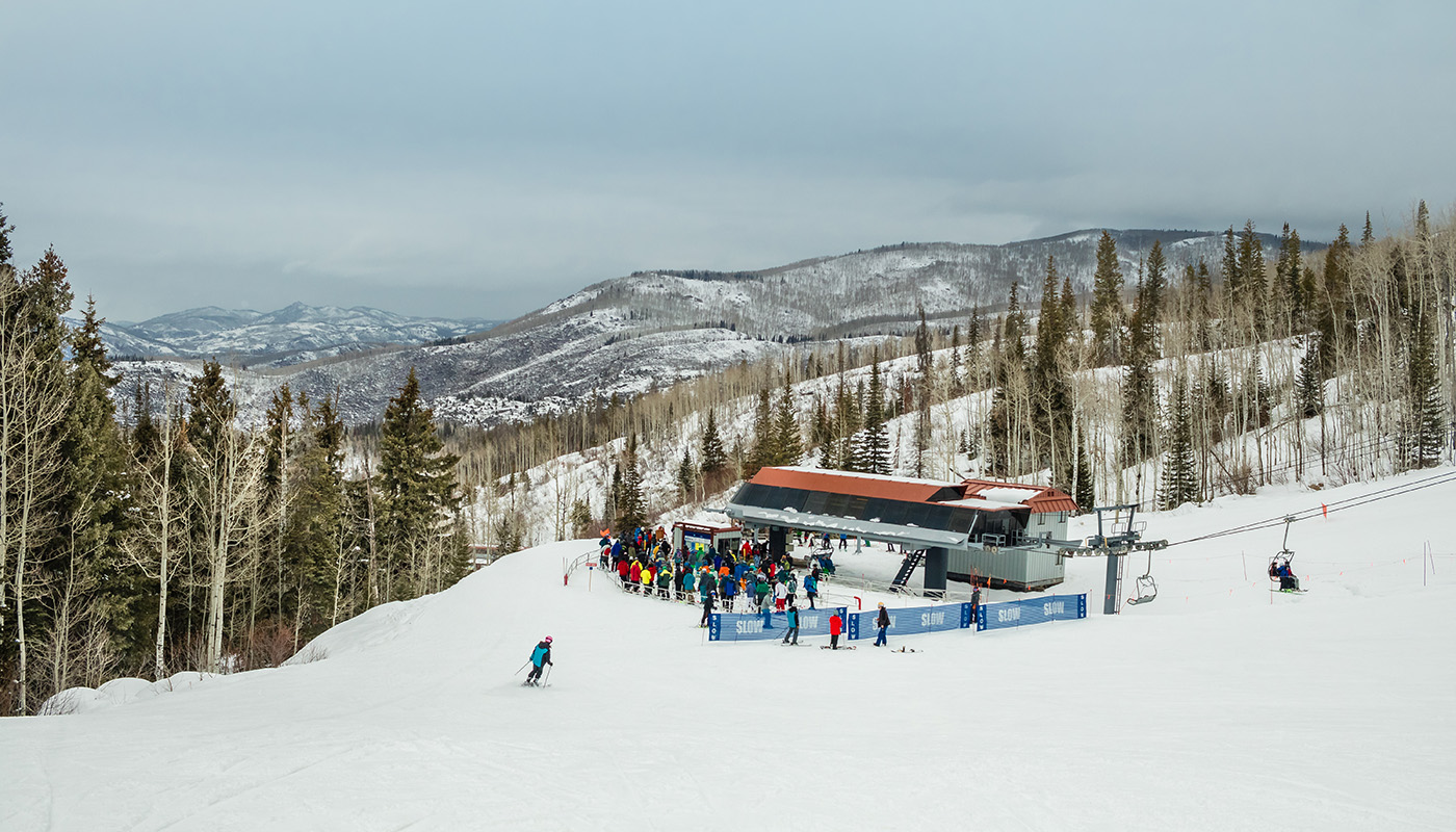 View of chair lift at the bottom of ski slope with skiers and snowboarders waiting to go up in Steamboat Springs, Colorado