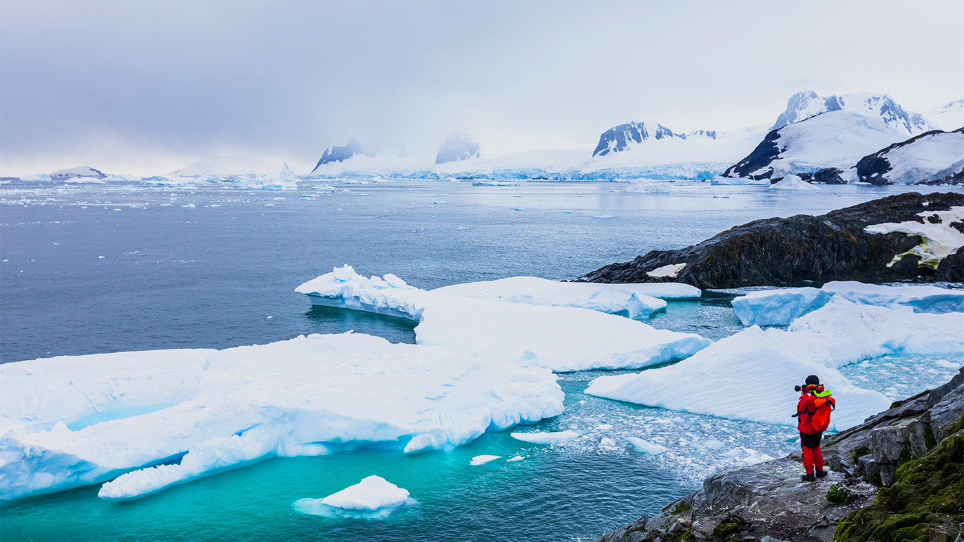 Tourist taking photos of amazing frozen landscape in Antarctica with icebergs, snow, mountains and glaciers, beautiful nature in Antarctic Peninsula with ice