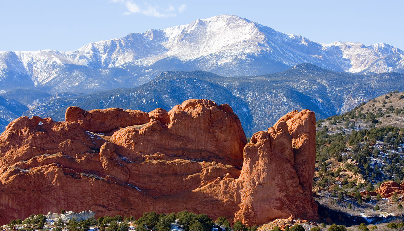 A large formation of red rocks sits in front of a snowy mountain range. 