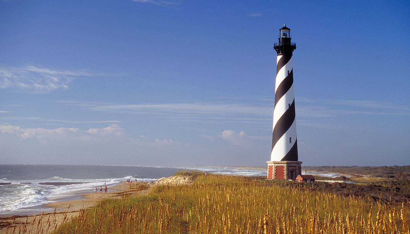 A lighthouse with black and white stripes near a beach in Outer Banks, North Carolina.