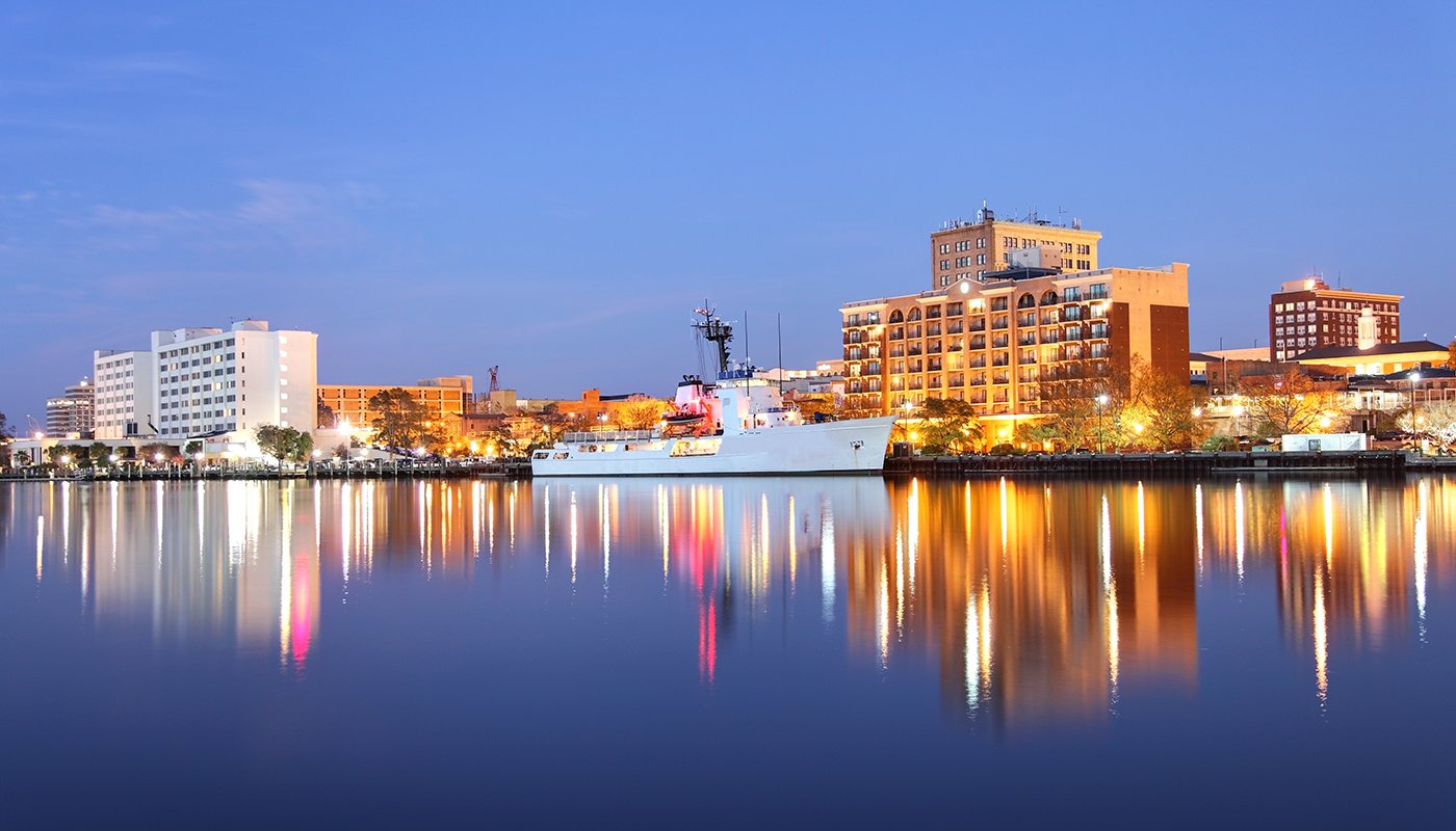 A large ship is docked beside tall buildings lit up at night in Wilmington, North Carolina.