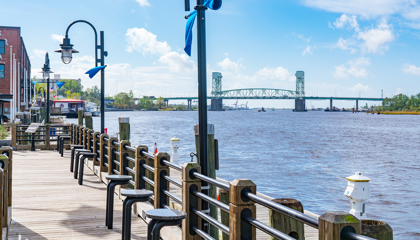 A view of the Wilmington Riverwalk with a bridge in the background.