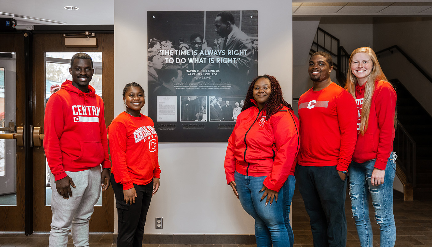 Four students in red Central College sweatshirts stand in front of MLK display