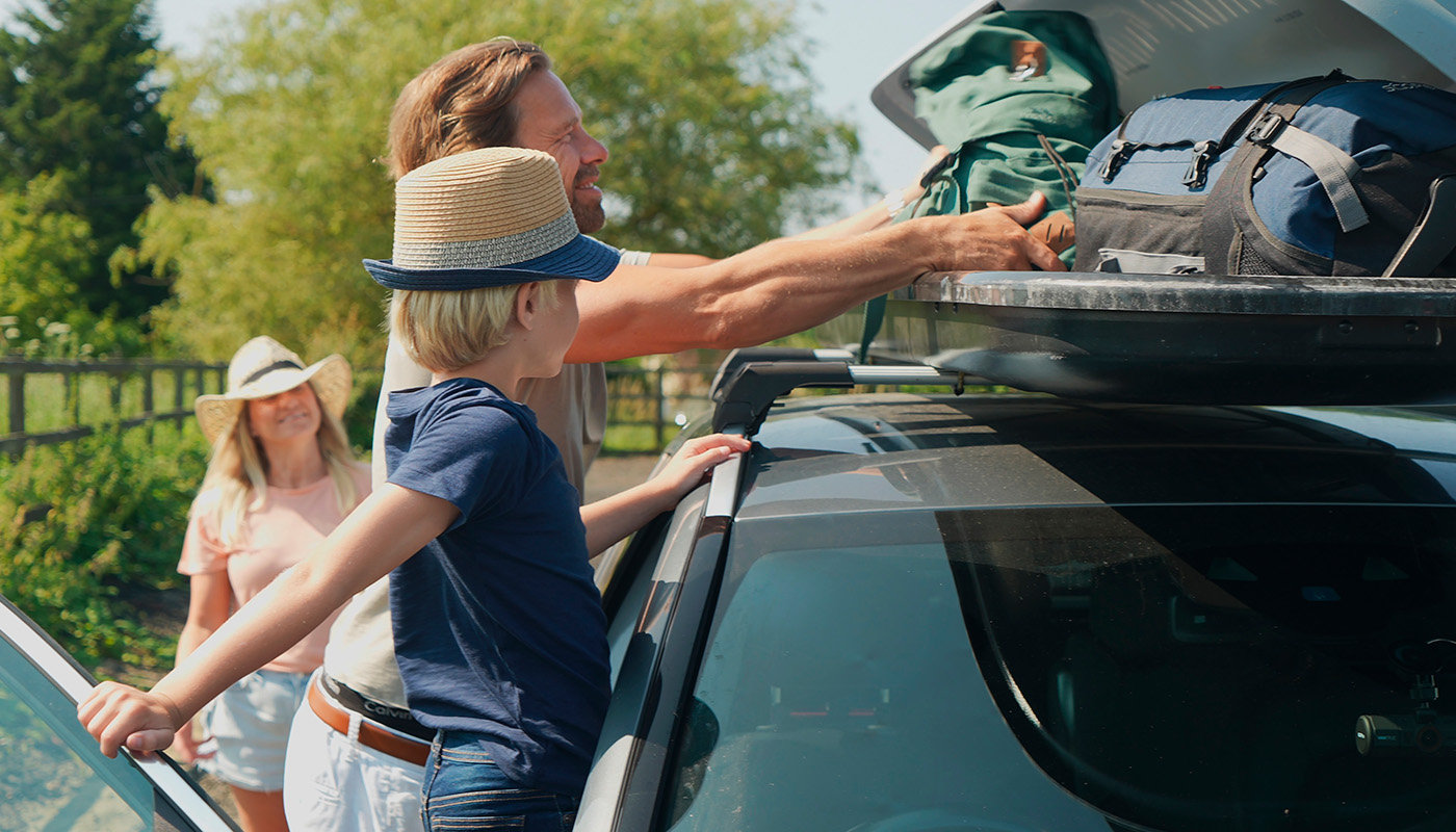Family loading luggage onto top of car in the English countryside